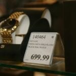 Gold watch with black dial, price tag.